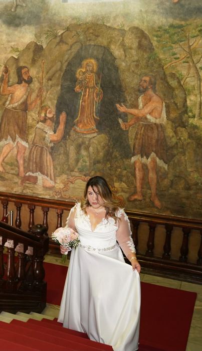 Novia con vestido blanco de encaje y fajín subiendo una escalera con un gran mural